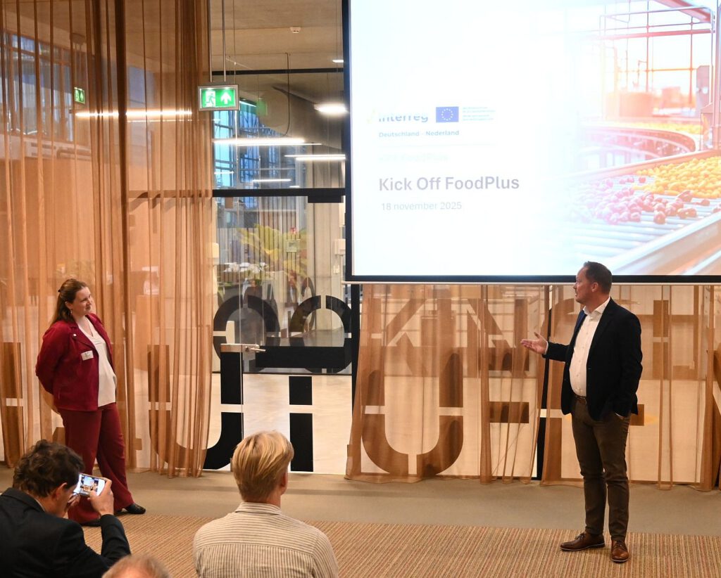 eine Frau und ein Mann stehen vor einer Leinwand und sprechen zum Saal - es ist das Kick Off FoodPlus