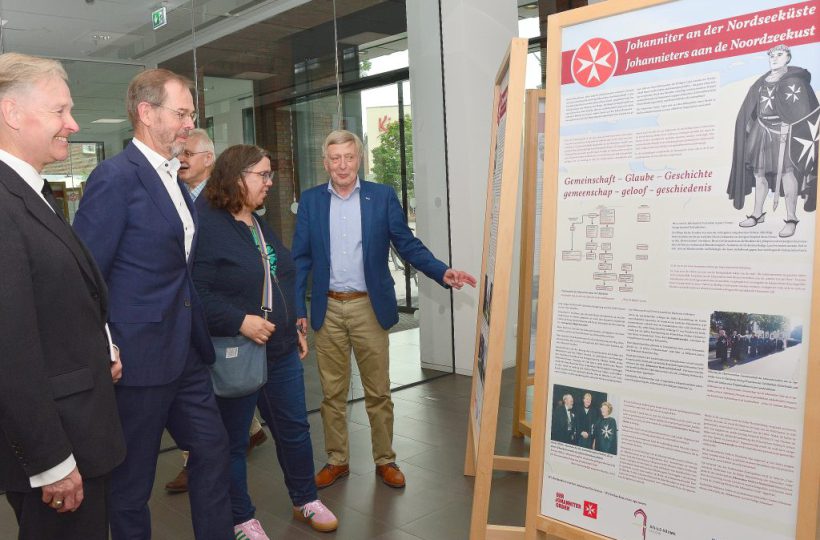 Fünf Menschen stehen vor einer Ausstellungstafel zum Thema "Johanniter an der Nordseeküste".