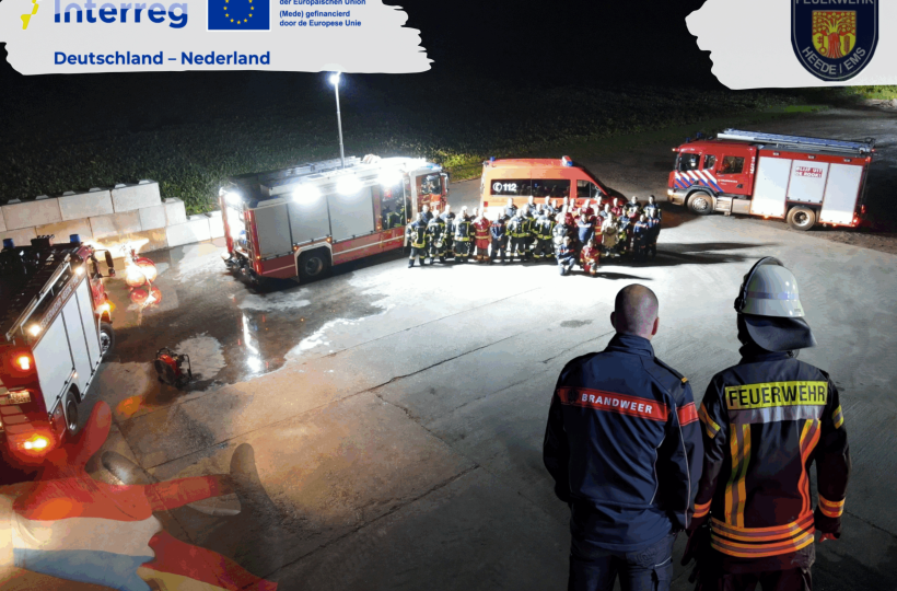 Gruppenfoto Feuerwehrleute aus Vogelperspektive. Im Vordergrund zwei Menschen mit je einer deutschen und einer niederländischen Feuerwehrkleidung. Interreg-Logo, Logo der Freiwilligen Feuerwehr Heede.
