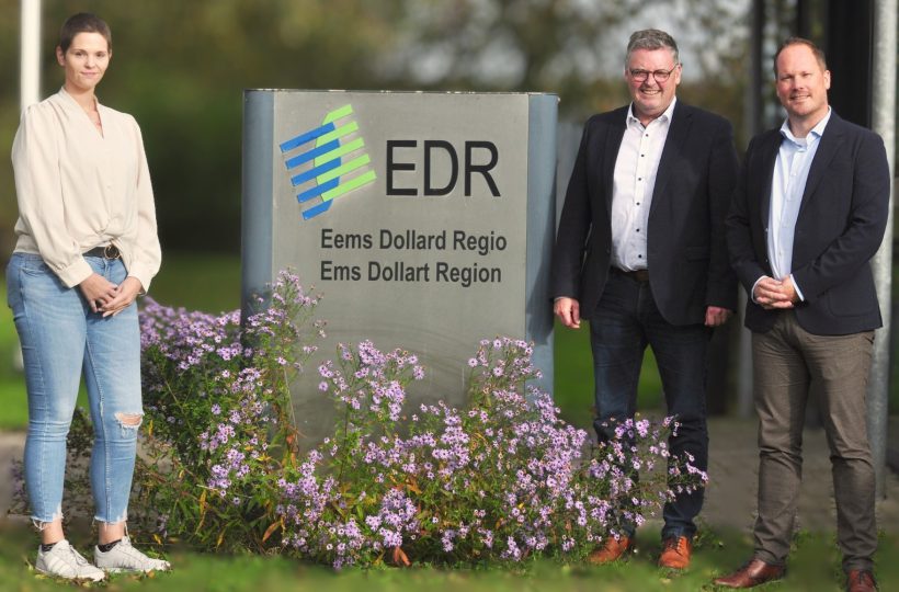 Auf dem Bild sind drei Personen am Schild der Ems Dollart Region zu sehen. Eine Frau und zwei Männer. Sie freuen sich über das gute Gespräch.